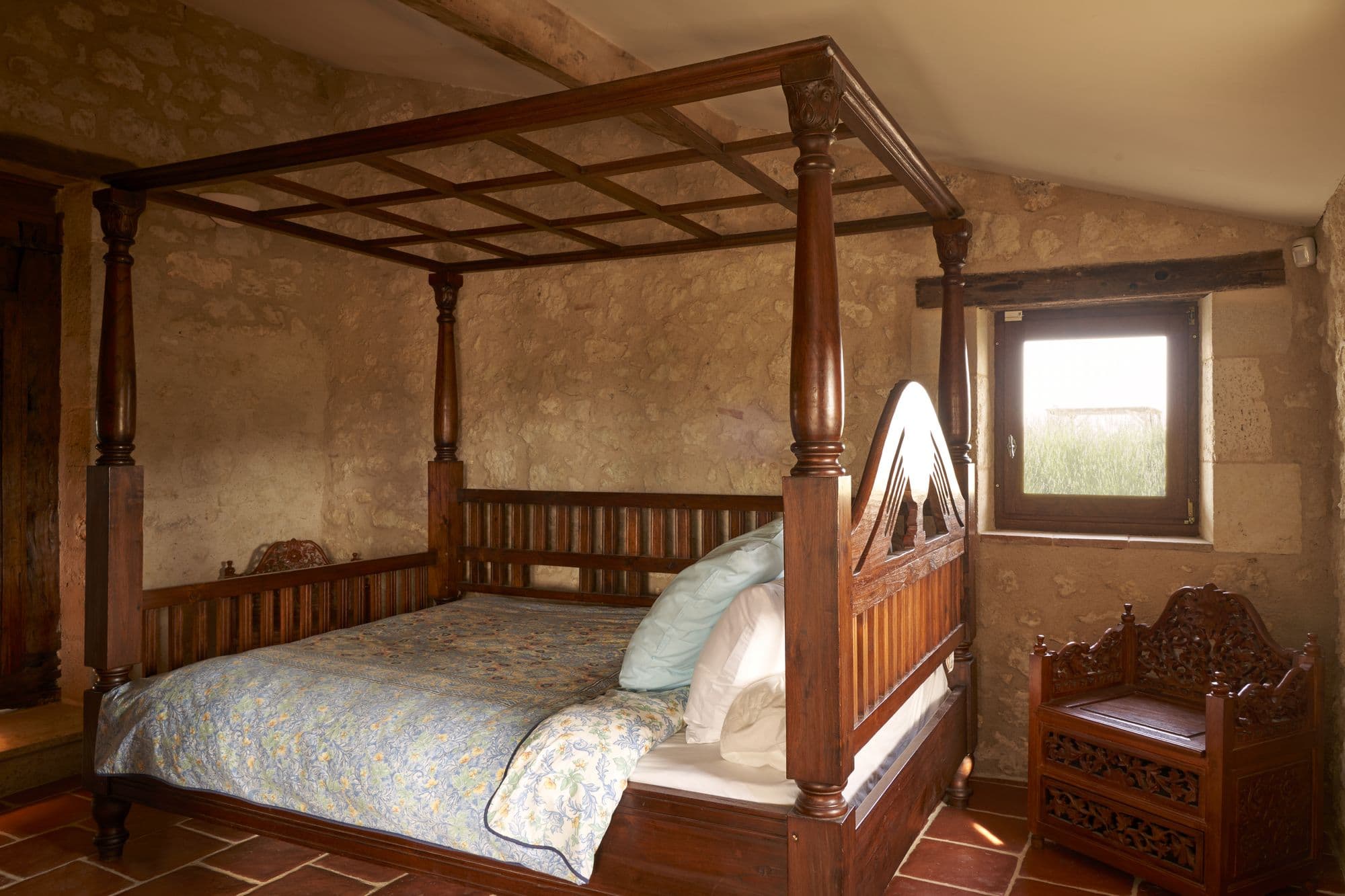 A bedroom with a carved four-poster bed against a stone wall