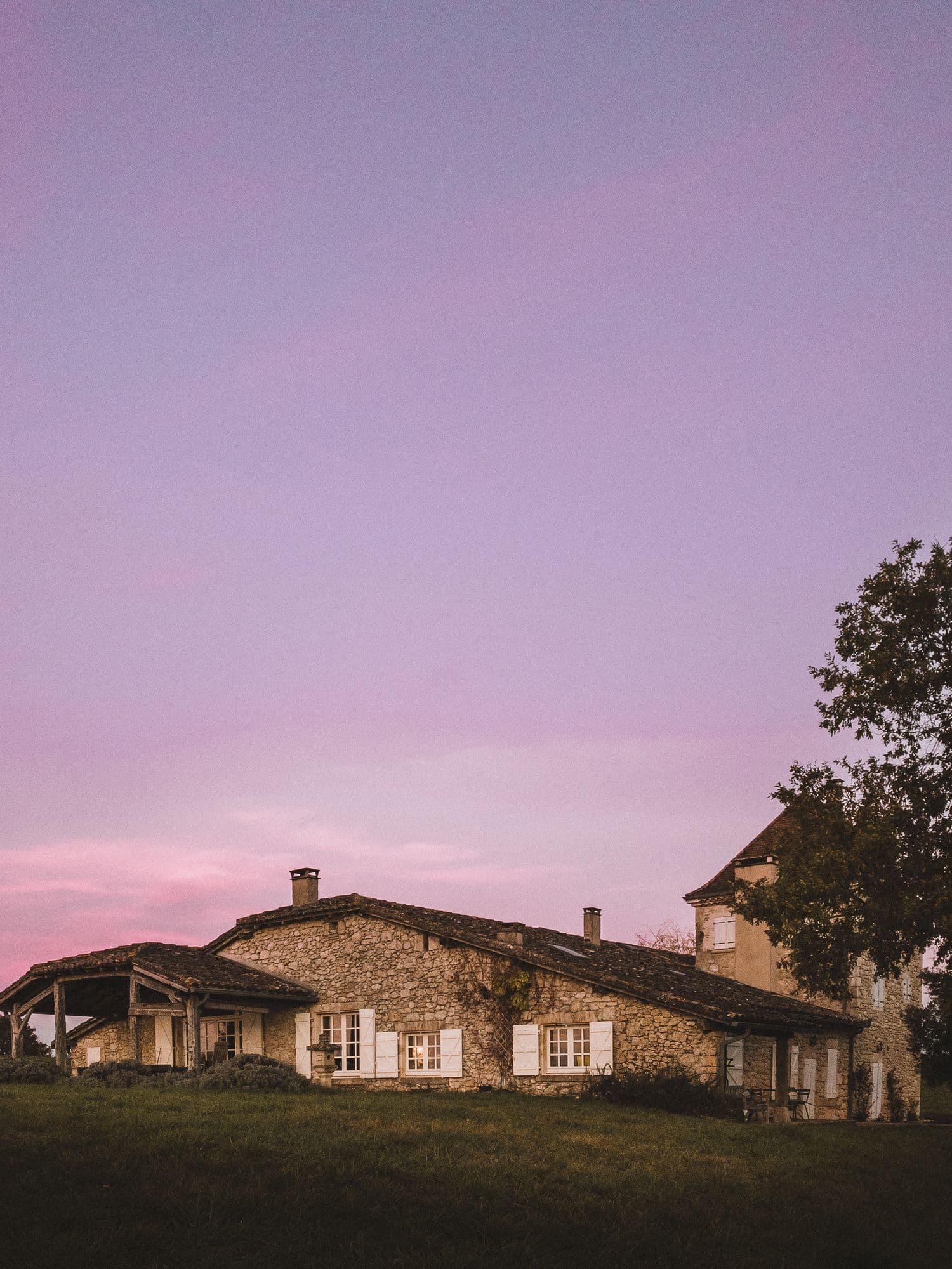 The farmhouse at dusk beneath a pink sky, its pigeonnier tower at one end