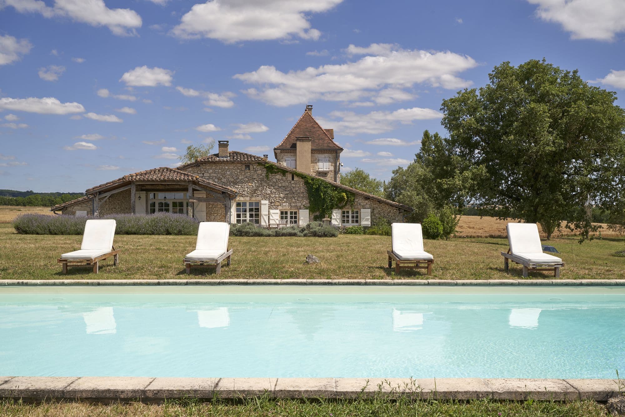 The pool in front of the house on a bright day, loungers along the lawn