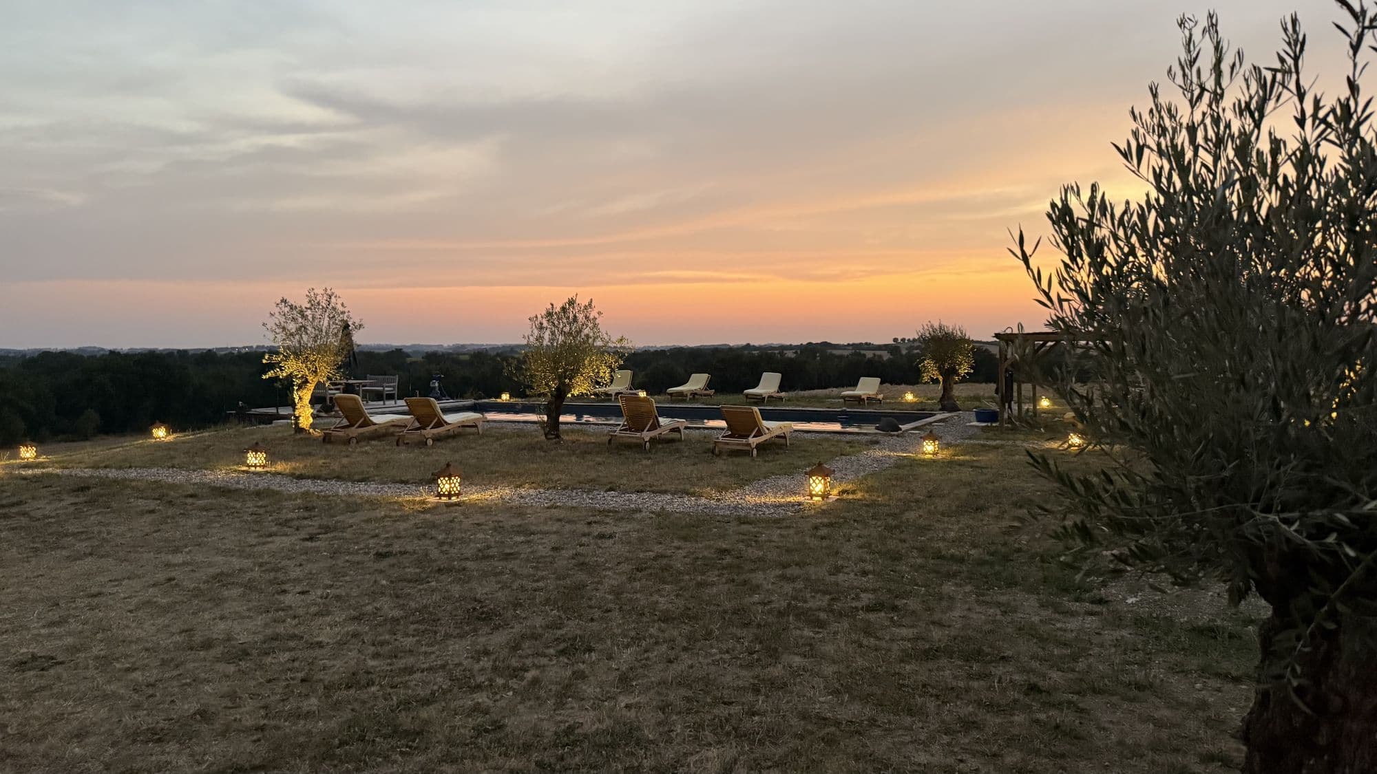 The pool at dusk with lanterns lit along the gravel and the last colour in the sky