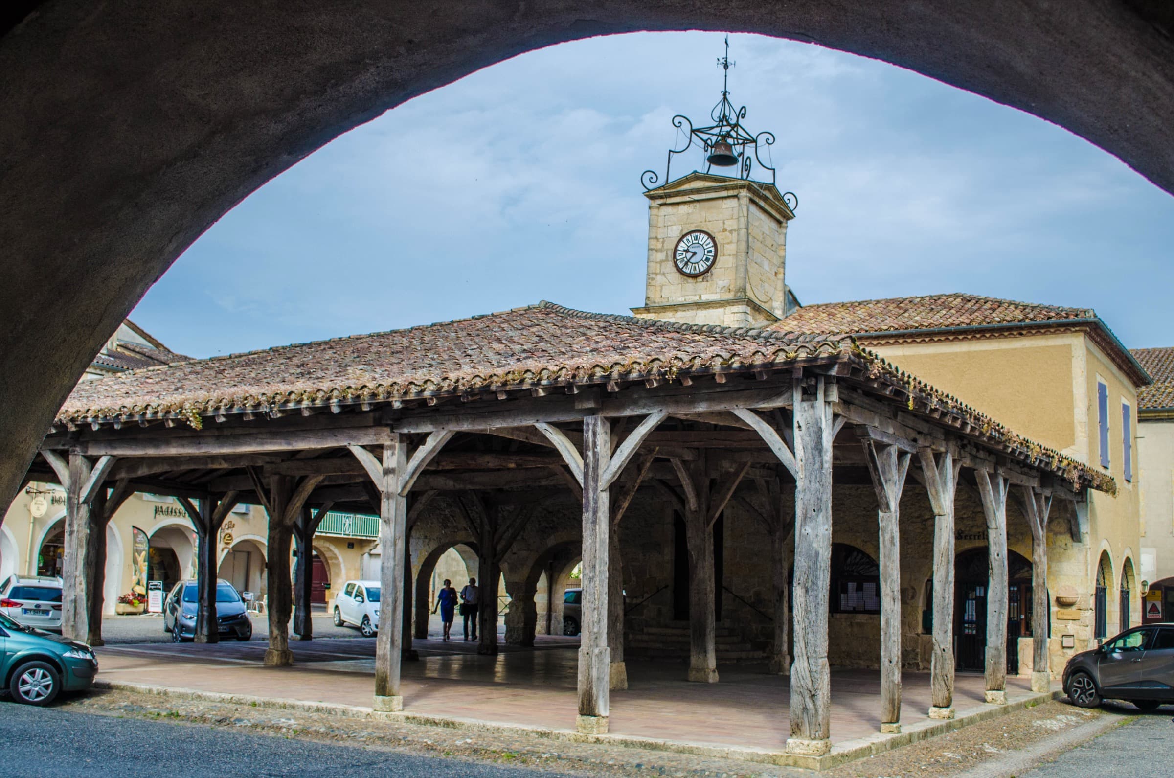 The timber market hall at Saint Clar seen through a stone arcade arch across the square