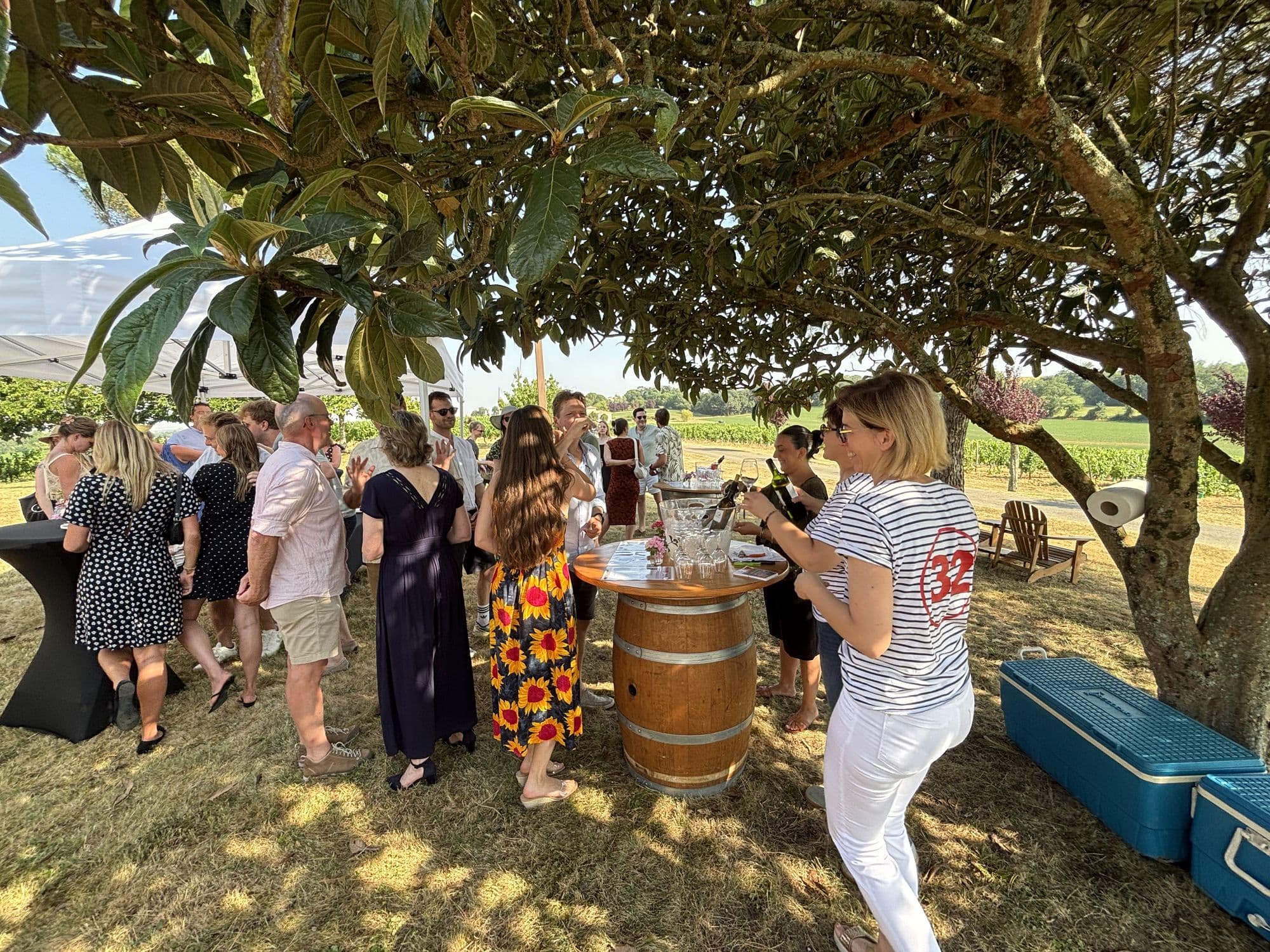Guests standing with drinks around wine-barrel tables under a tree